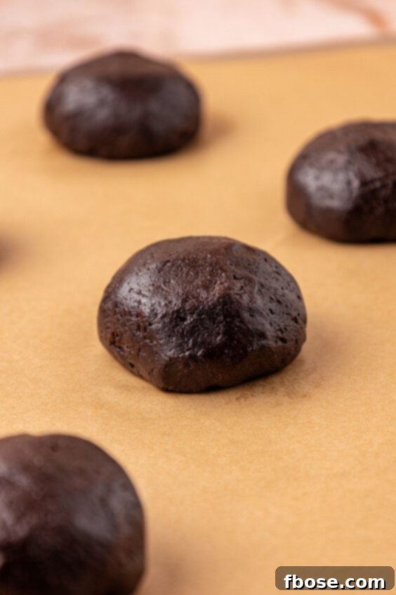 Chocolate cookie dough balls on a parchment lined baking sheet.