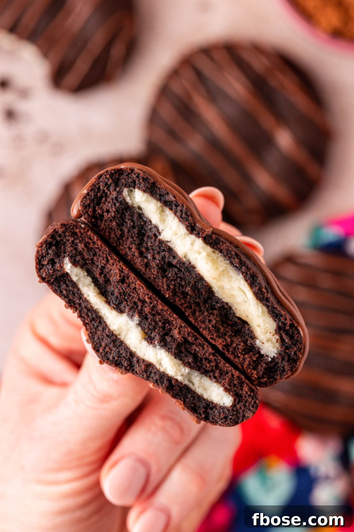 A woman's hand holding a cookie split in half to show the cheesecake filling.