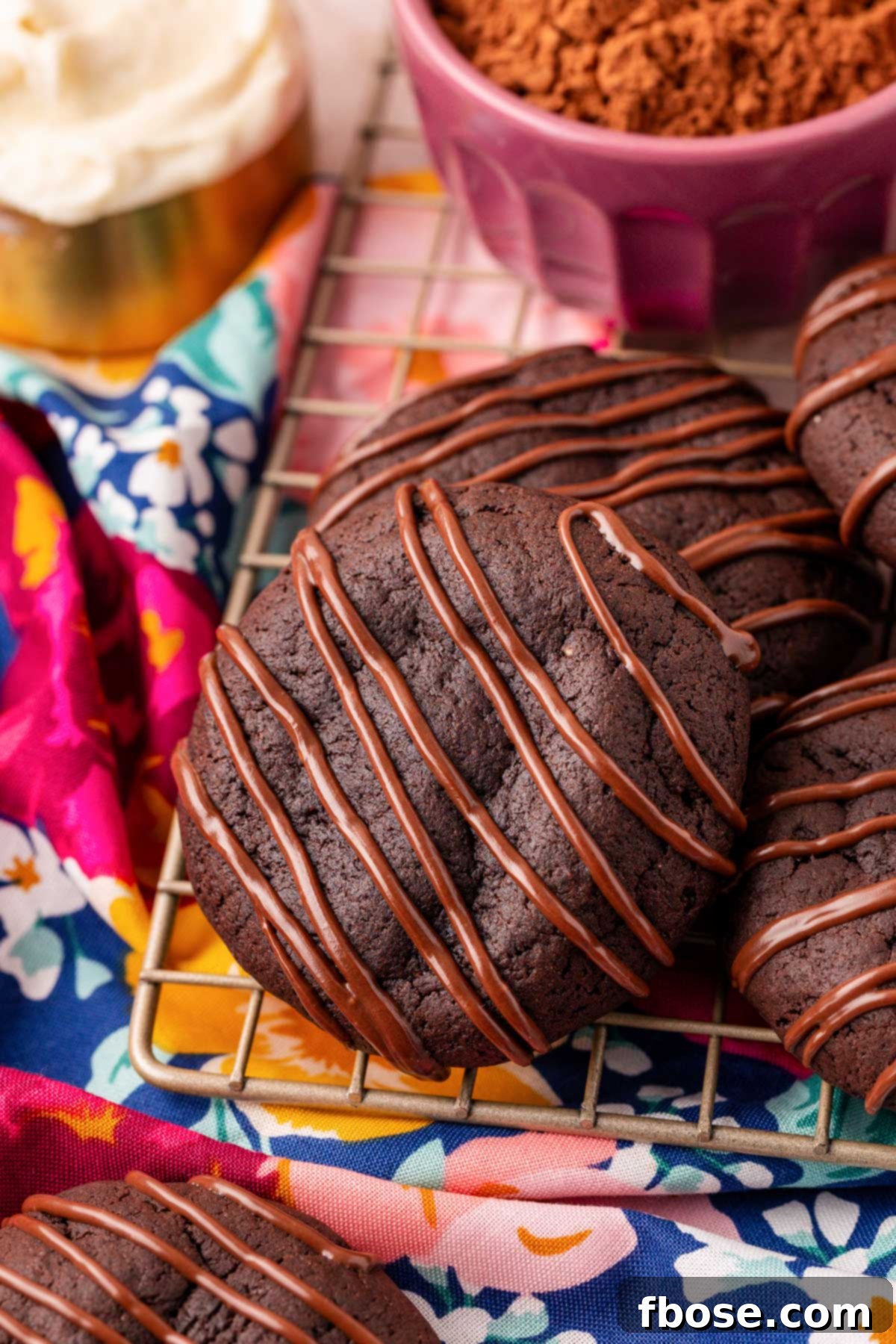 Chocolate cookies with chocolate drizzle on a wire cooling rack.
