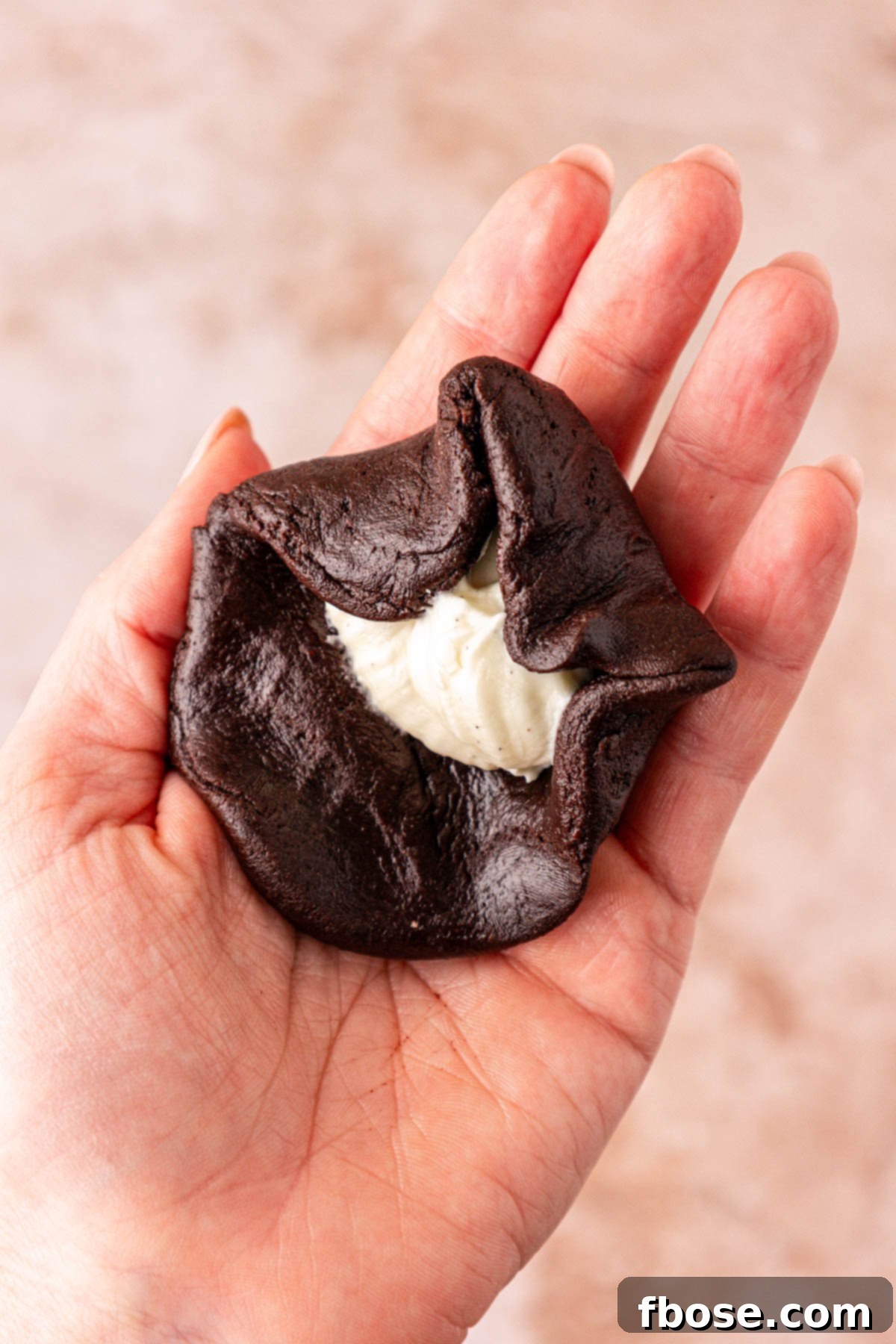 Chocolate cookie dough being wrapped around cream cheese in a woman's hand to make cookies.
