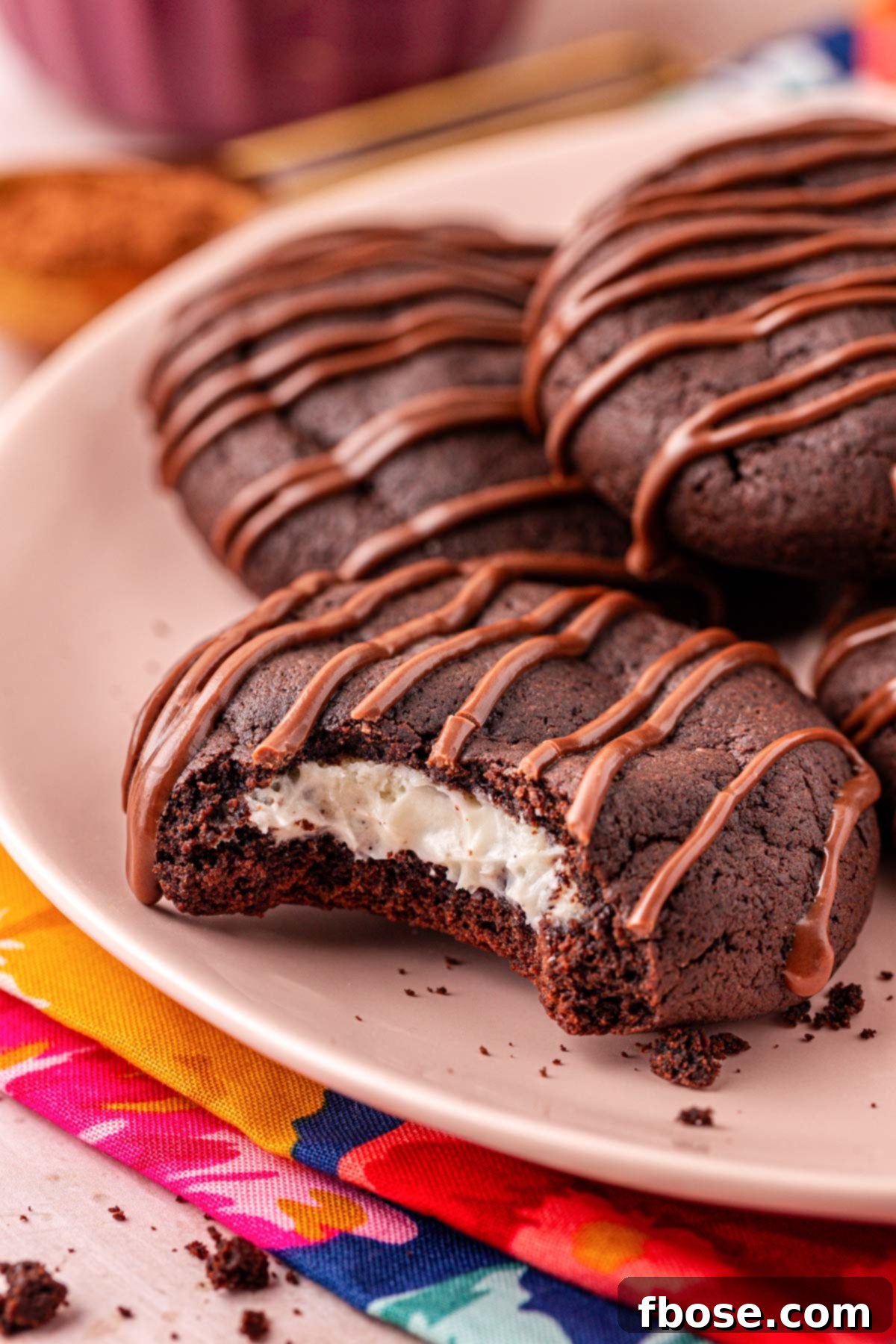 Close up of a chocolate cookie with cream cheese filling on a pink plate with a bite missing.