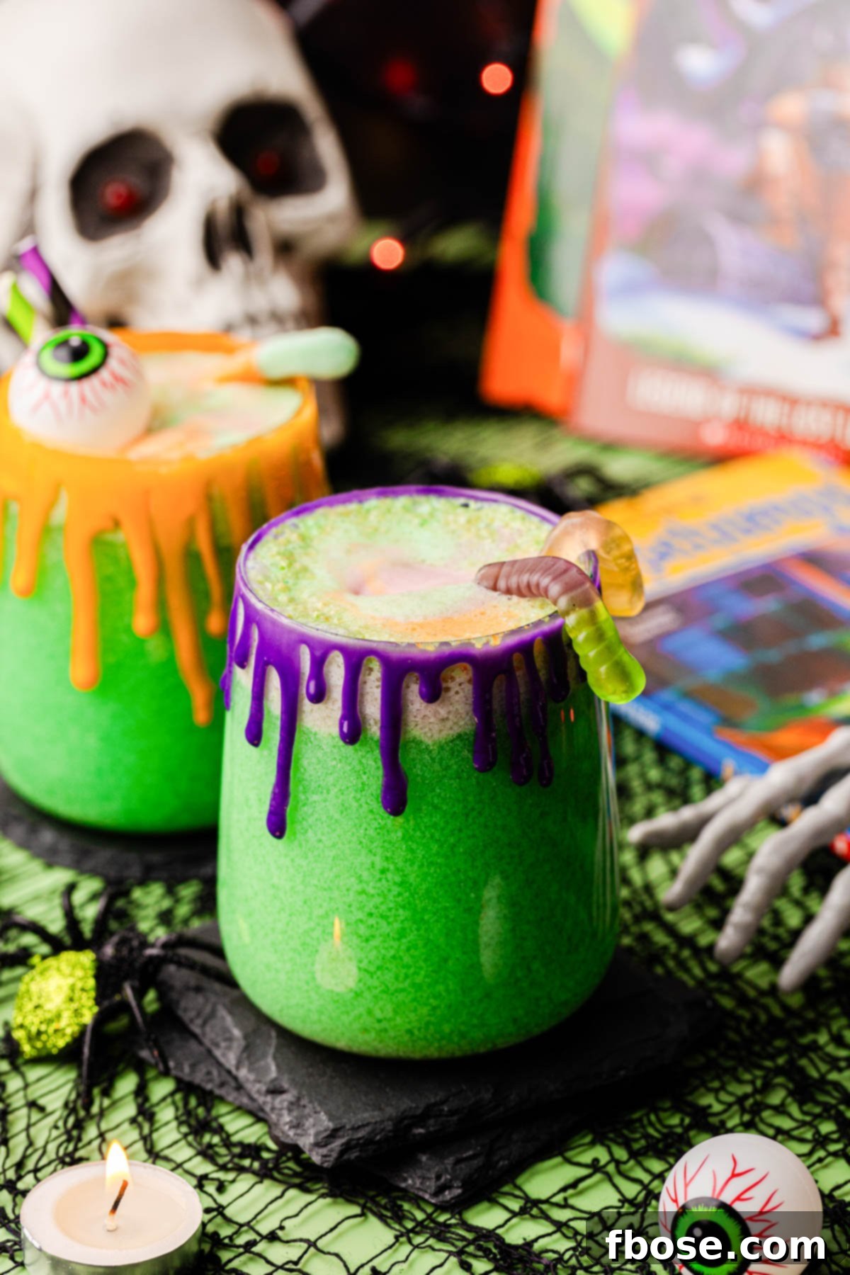 Two glasses of vibrant green Goosebumps punch for Halloween, decorated with gummy worms and spooky elements, set on a festive table.