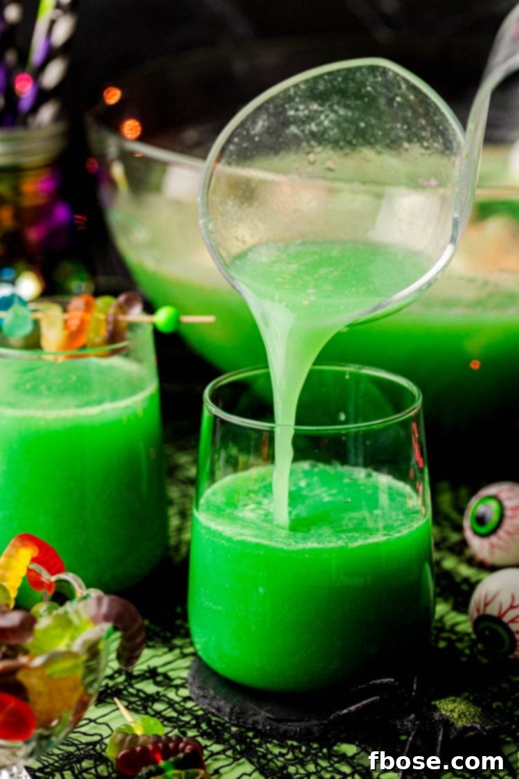 Green Halloween punch being ladled into individual glasses, garnished with gummy worms.
