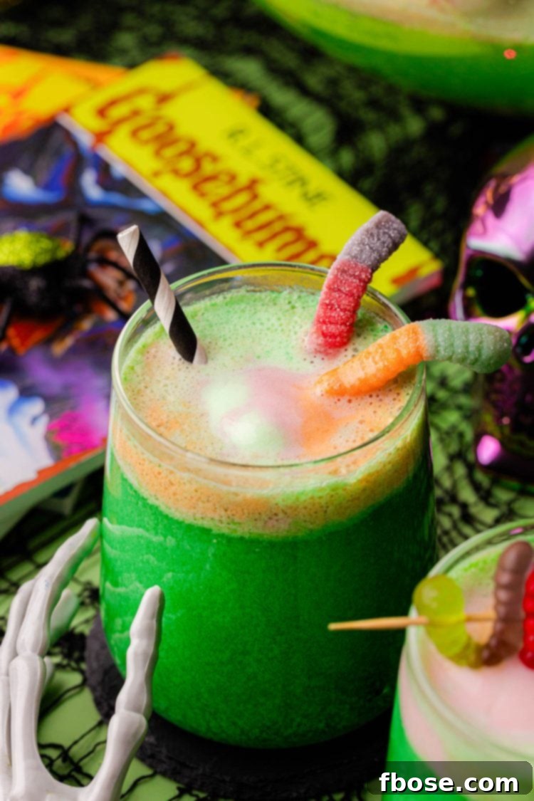 Two hands holding glasses of green Halloween punch with gummy worms.
