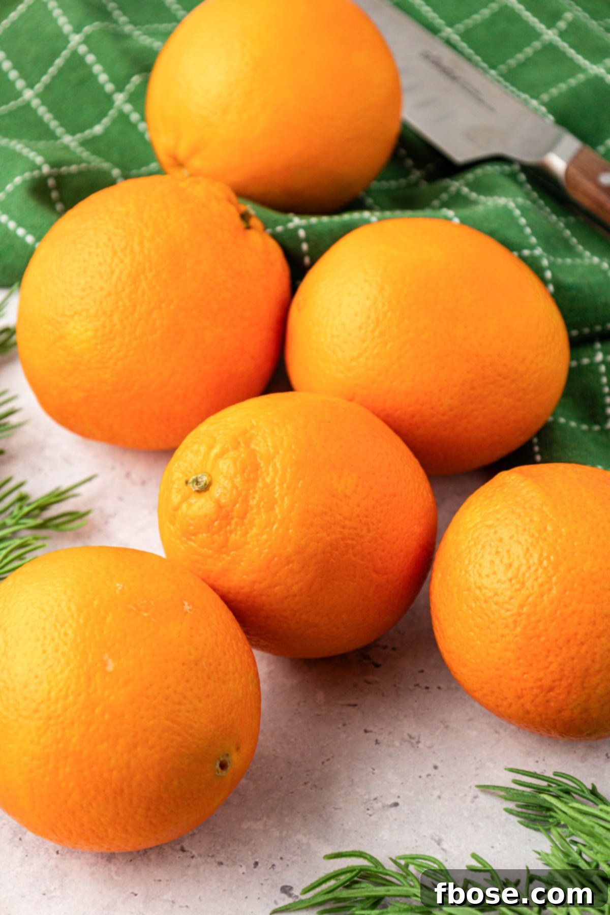 Oven-Dried Orange Slices 3 Fresh oranges arranged beautifully on a wooden table with a soft green linen napkin.
