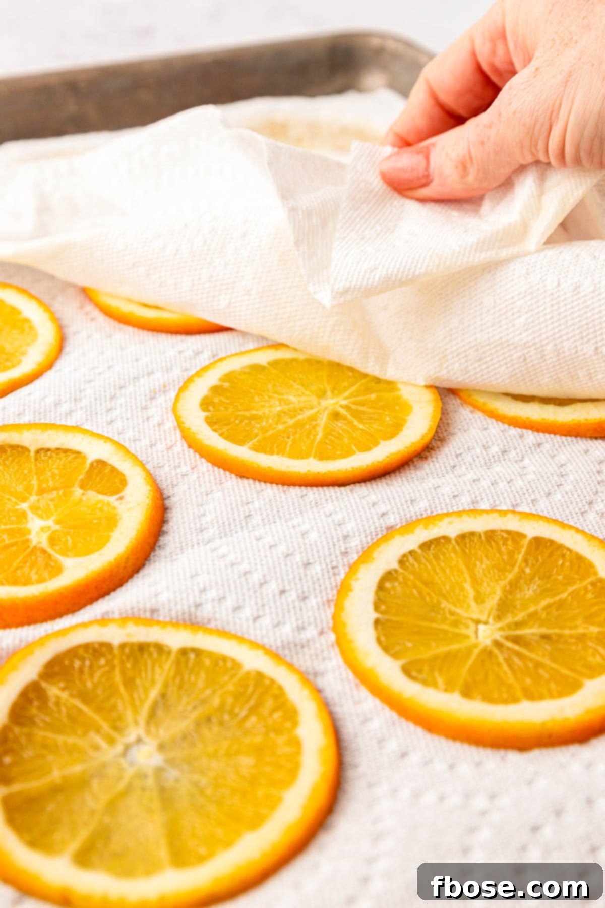 Oven-Dried Orange Slices 5 A woman's hand gently patting down thin orange slices with a paper towel to remove excess moisture.