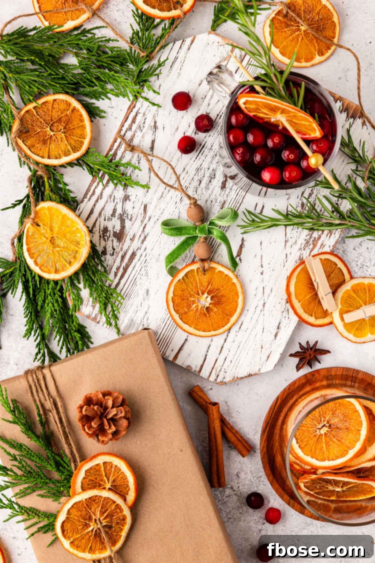 Oven-Dried Orange Slices 6 An overhead view of beautifully dried orange slices artfully arranged with various holiday decor elements and cocktail garnishes on a white table.