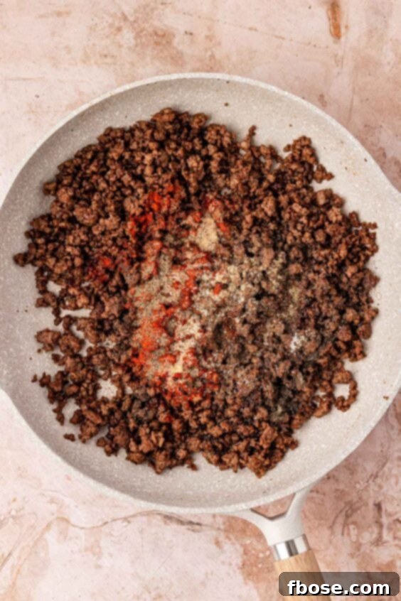 Spices being added to browned ground beef in a skillet.