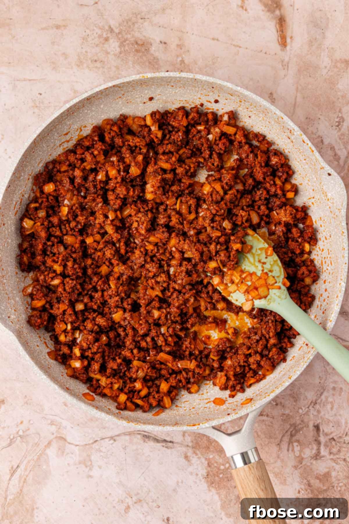 Ground beef with seasonings and onions simmering in a skillet.