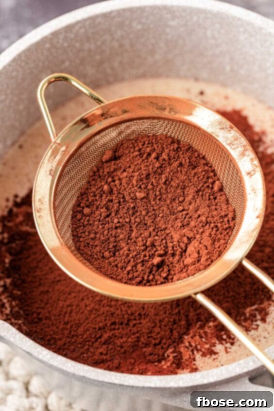 Cocoa powder being sifted carefully into a pot of warm milk and cream.