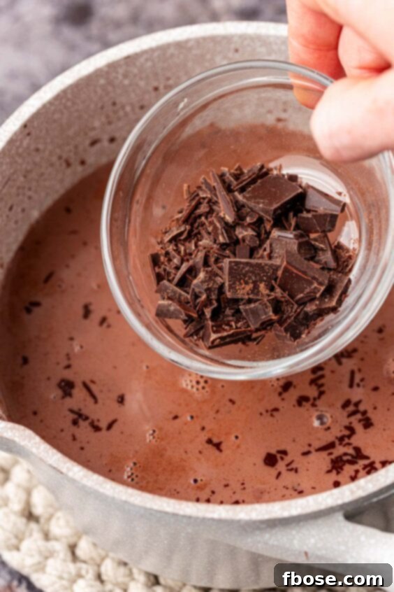 Finely chopped bittersweet chocolate being added to the hot chocolate base in a saucepan.