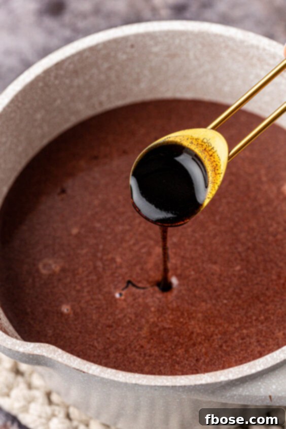 Vanilla bean paste being stirred into the chocolate mixture in a pot.