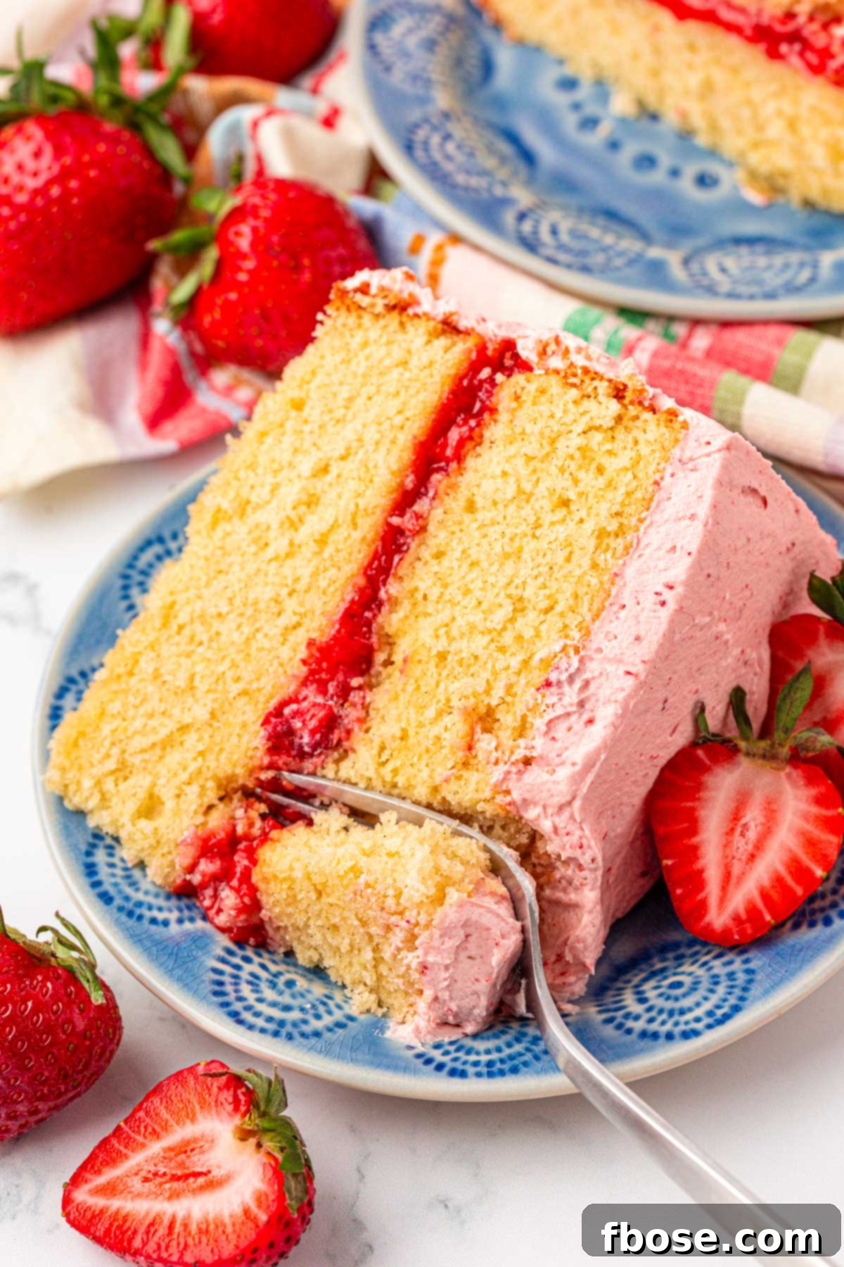 Close up photo of a slice of strawberry vanilla cake with a fork taking a bite from it.