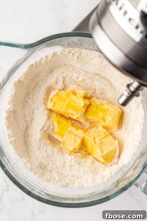 Softened butter being added to flour and sugar in a mixing bowl.