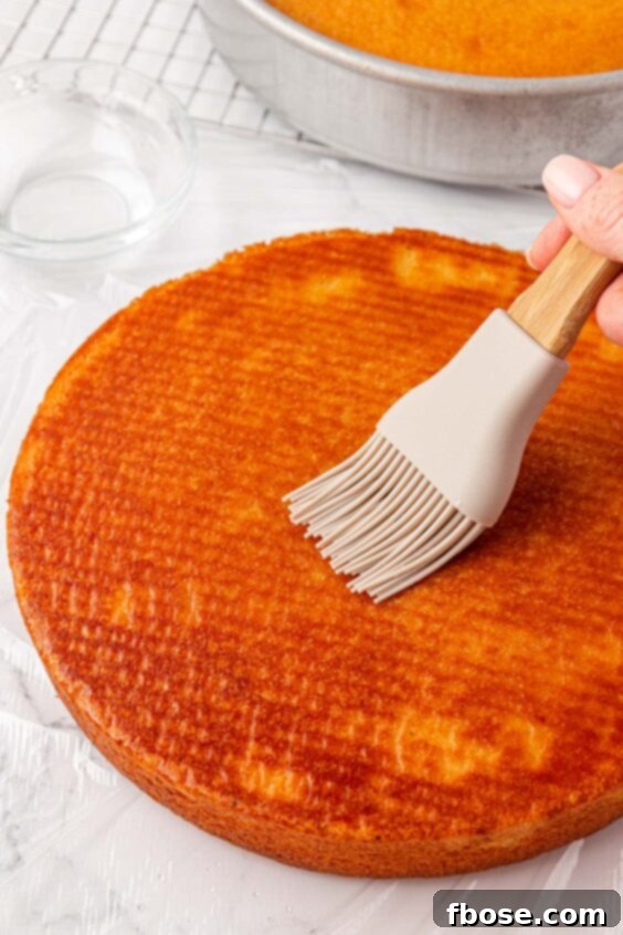 A silicone brush brushing vanilla cake with simple syrup.