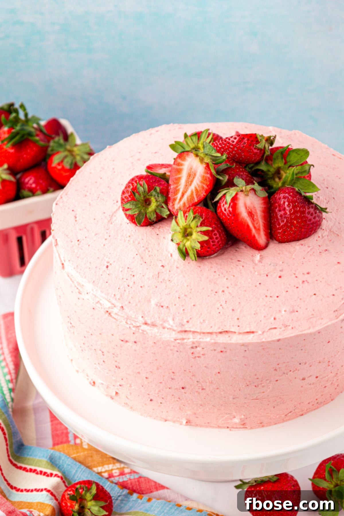Close up of a strawberry frosted cake on a white cake stand.