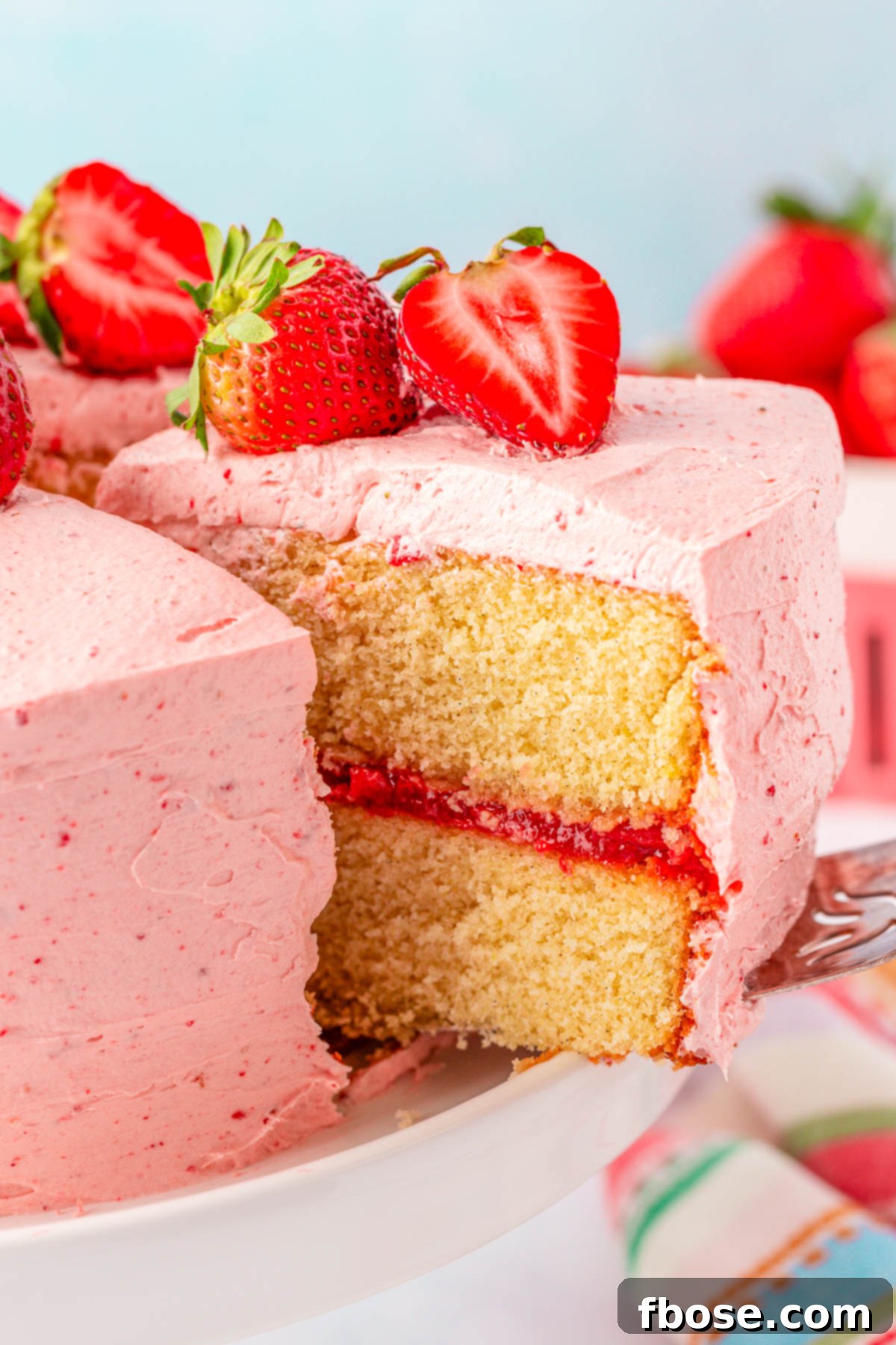 A slice of strawberry cake being lifted off a white cake stand.