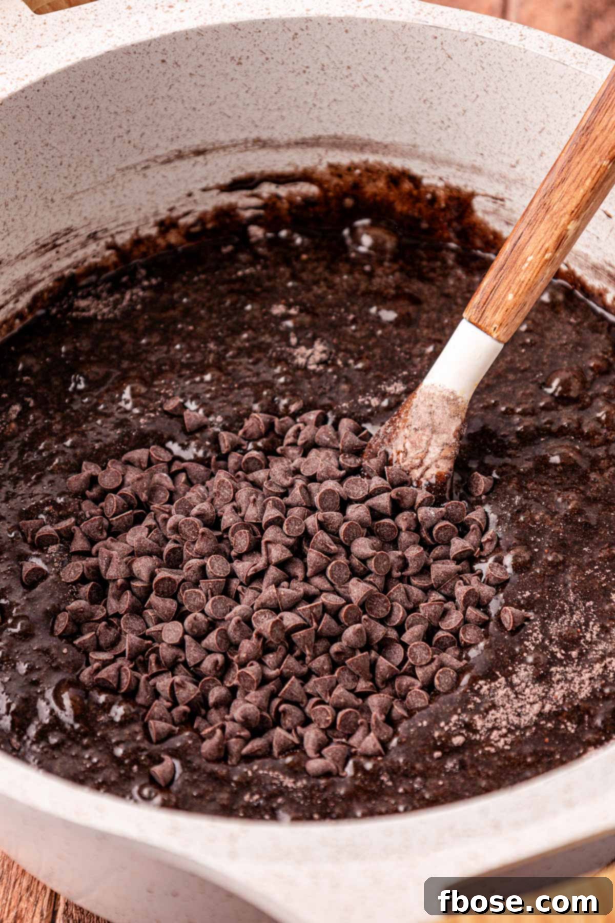 A pot of brownie batter with chocolate chips being folded in.