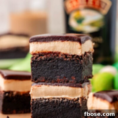 Two brownies with Irish cream frosting and ganache topping stacked on a piece of parchment paper.