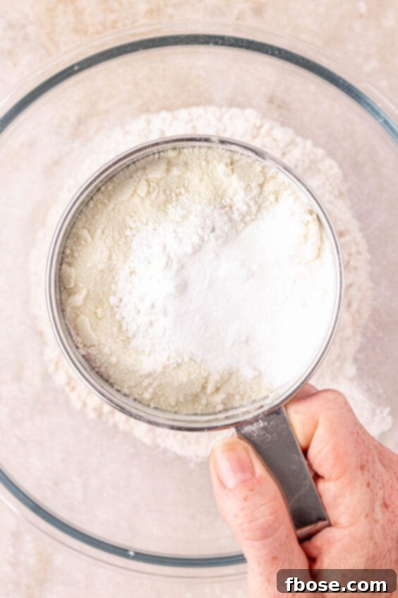 A woman's hand using a sifter for baking, preparing dry ingredients for cookie dough.
