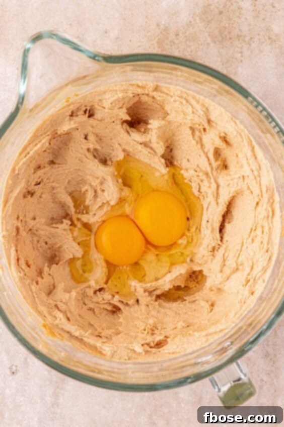 Two eggs being added to a mixing bowl to make cookie dough, illustrating the wet ingredient step.