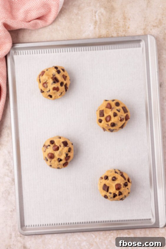 Baking sheet lined with parchment paper with 4 cookie dough balls on it, ready for the oven.