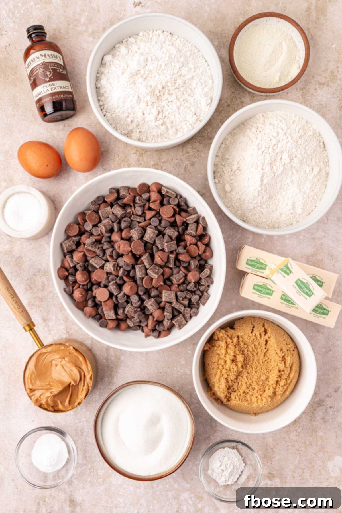 Overhead photo of ingredients to make peanut butter chocolate chip cookies laid out on a table, including flours, sugars, butter, and chocolate chips.