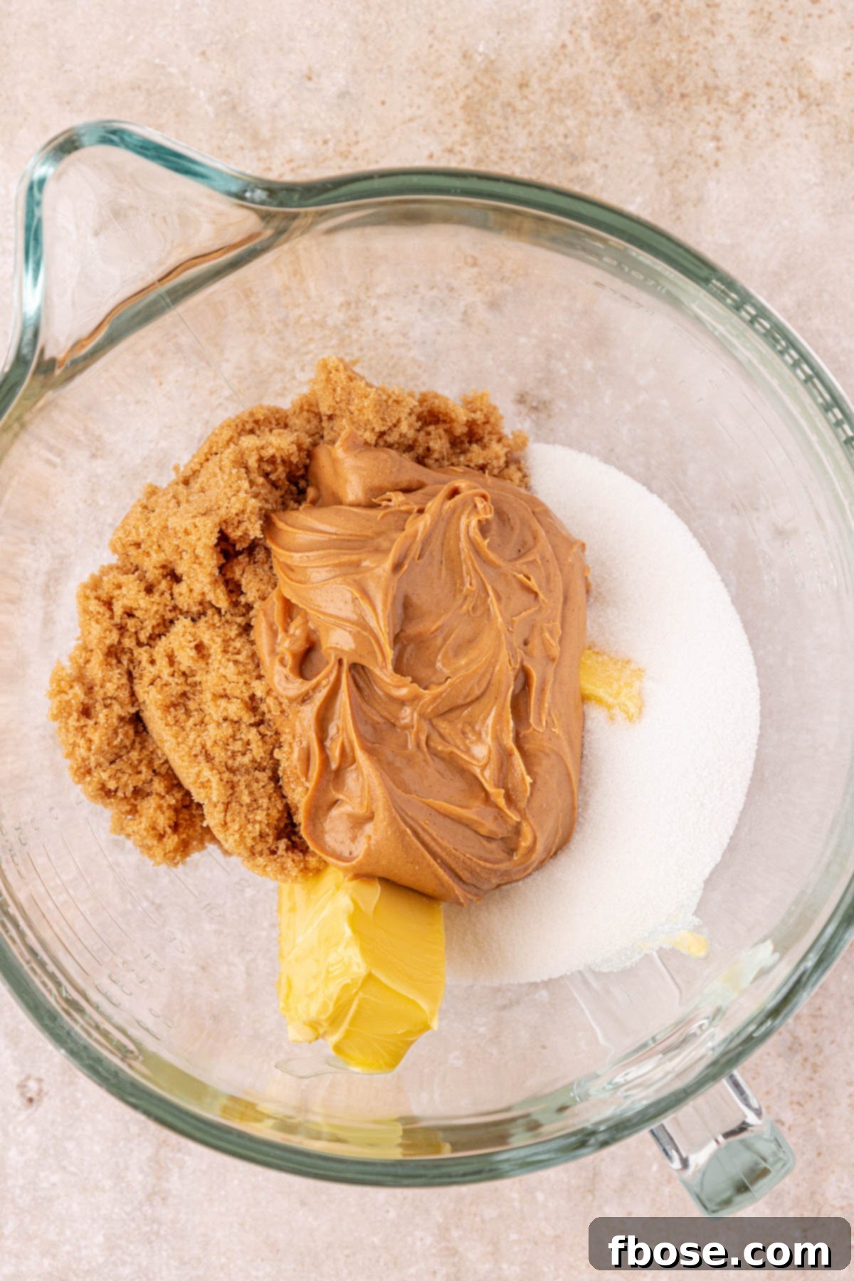 Peanut butter, butter, and sugar in a mixing bowl, ready to be creamed together for cookie dough.