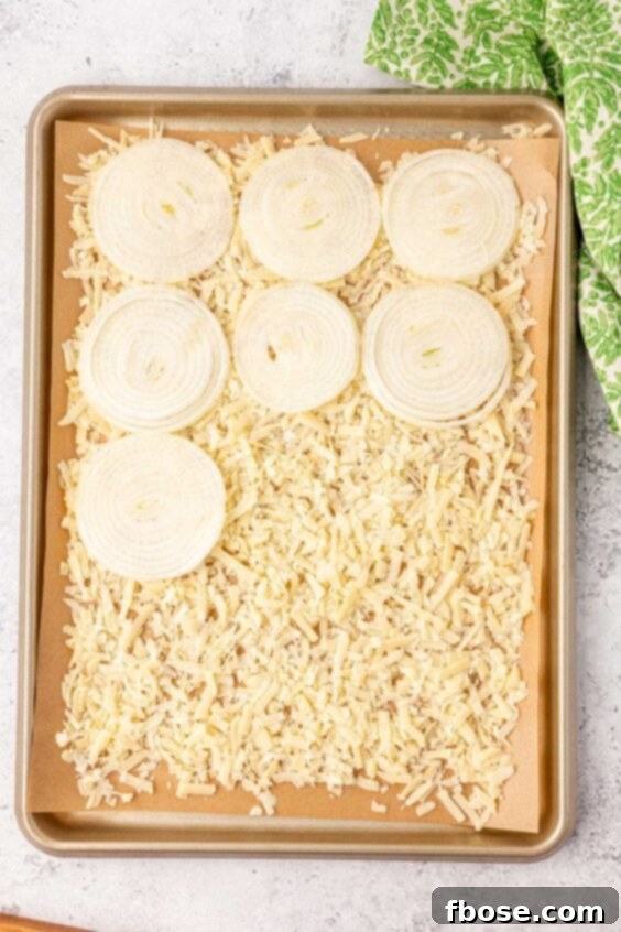 Onion slices on a bed of shredded parmesan on a pan.