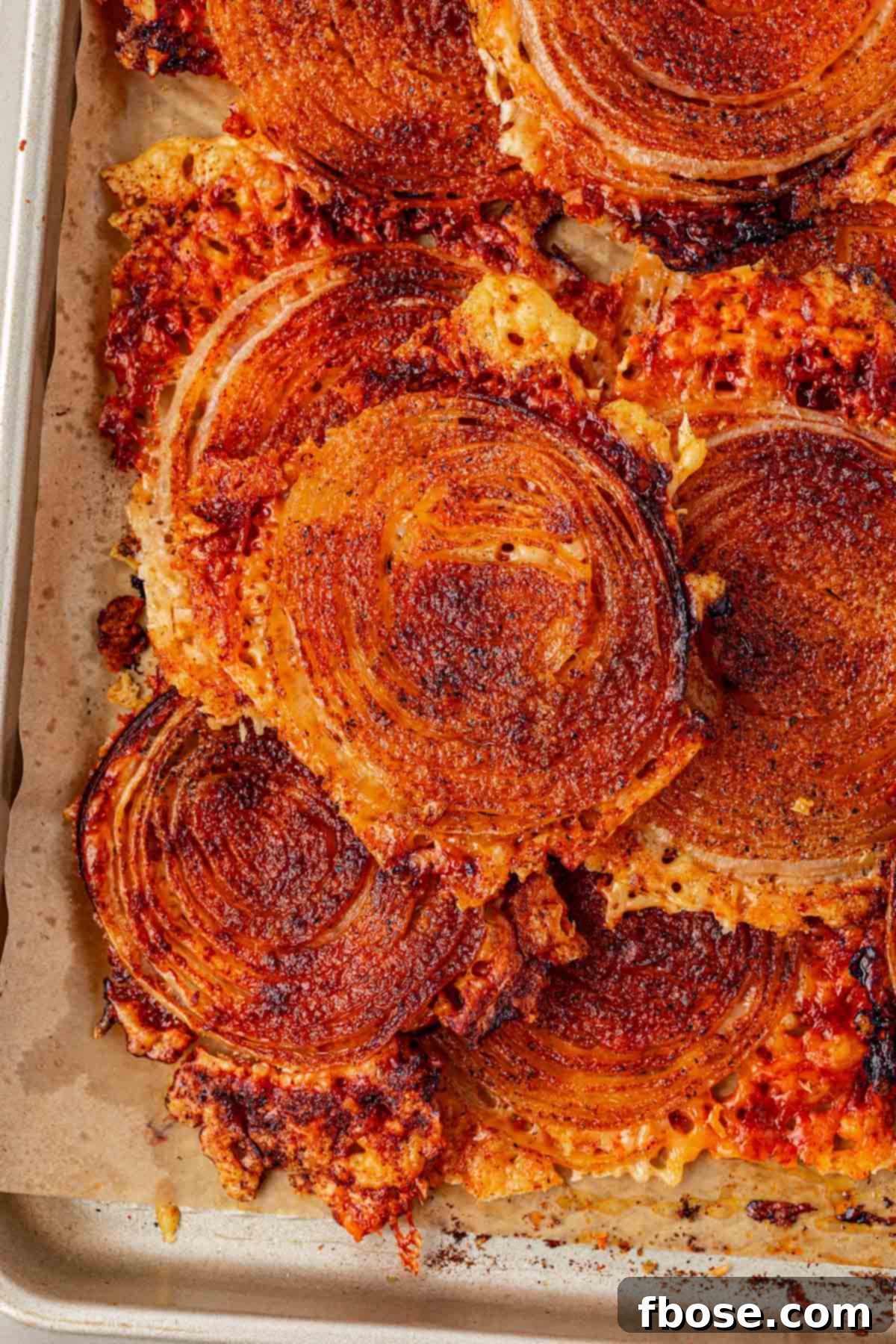 Golden, crispy onion ring chips cooling on a parchment-lined baking pan.