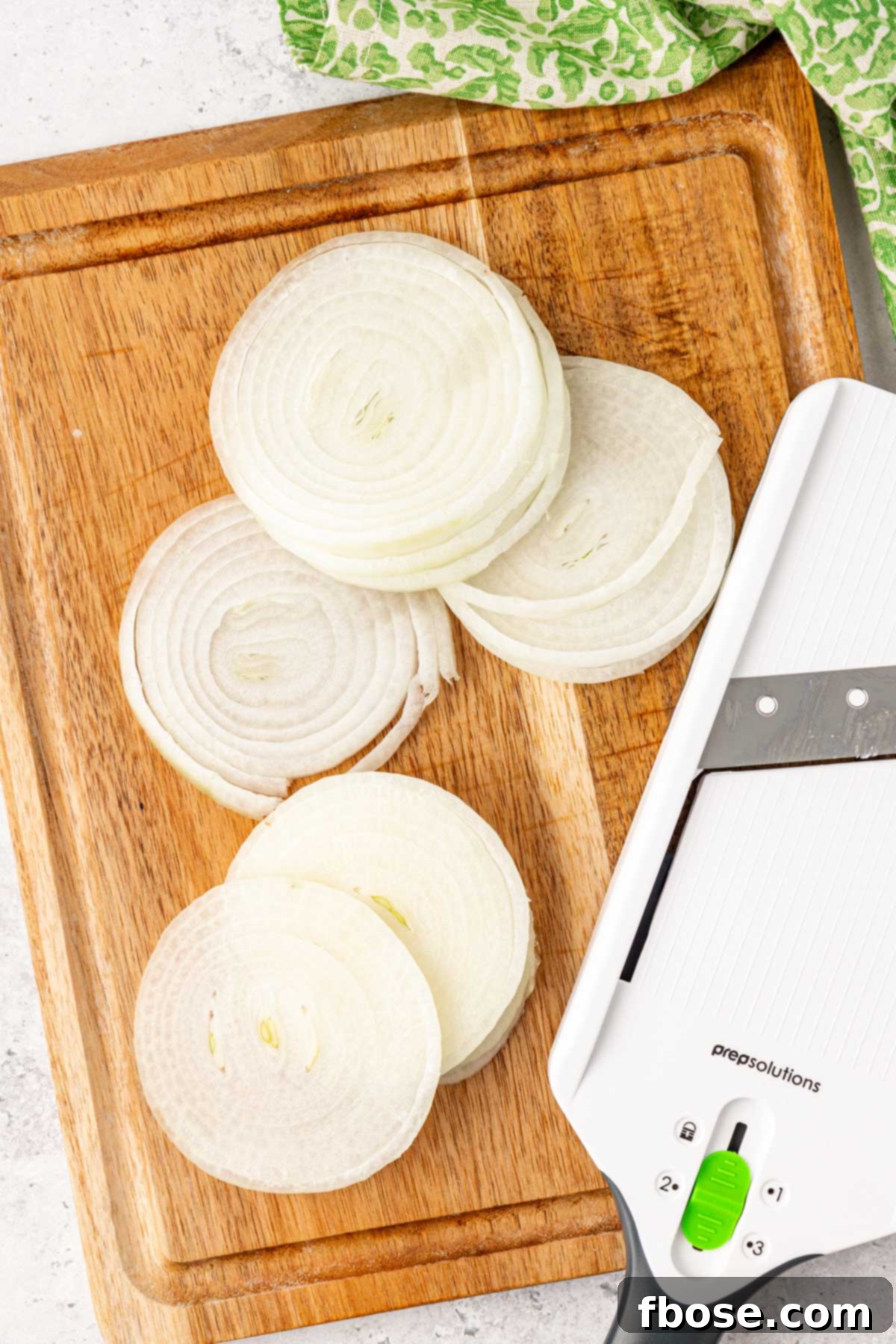Thinly sliced onions prepared on a mandolin and resting on a cutting board.