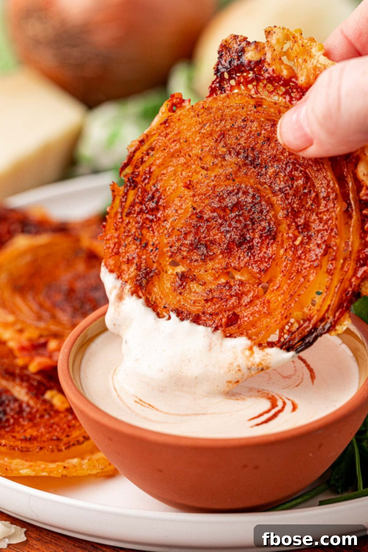 A hand dipping an onion ring chip into a creamy dressing.