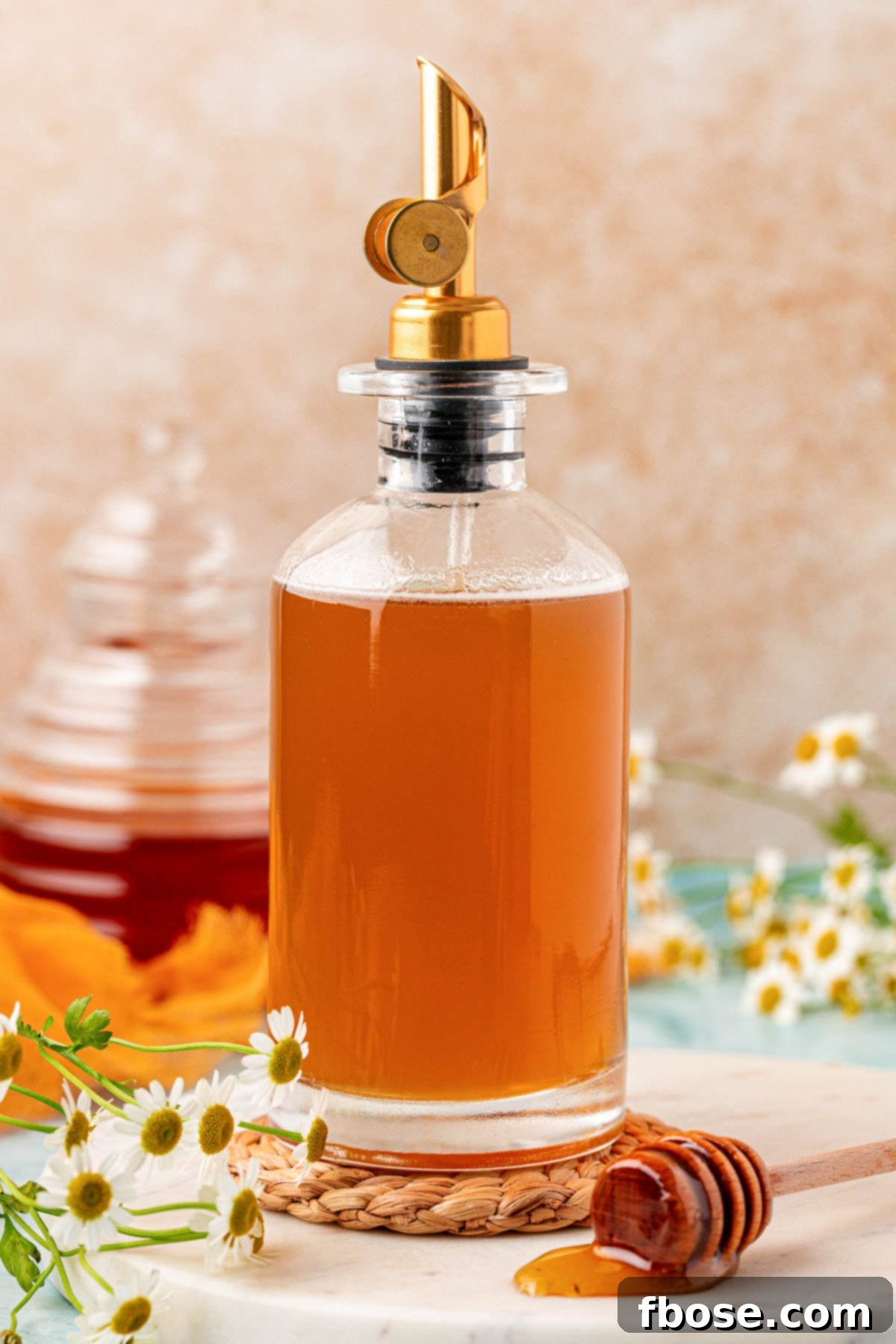A glass bottle of golden honey simple syrup on a rustic rope coaster, ready to be poured into drinks.