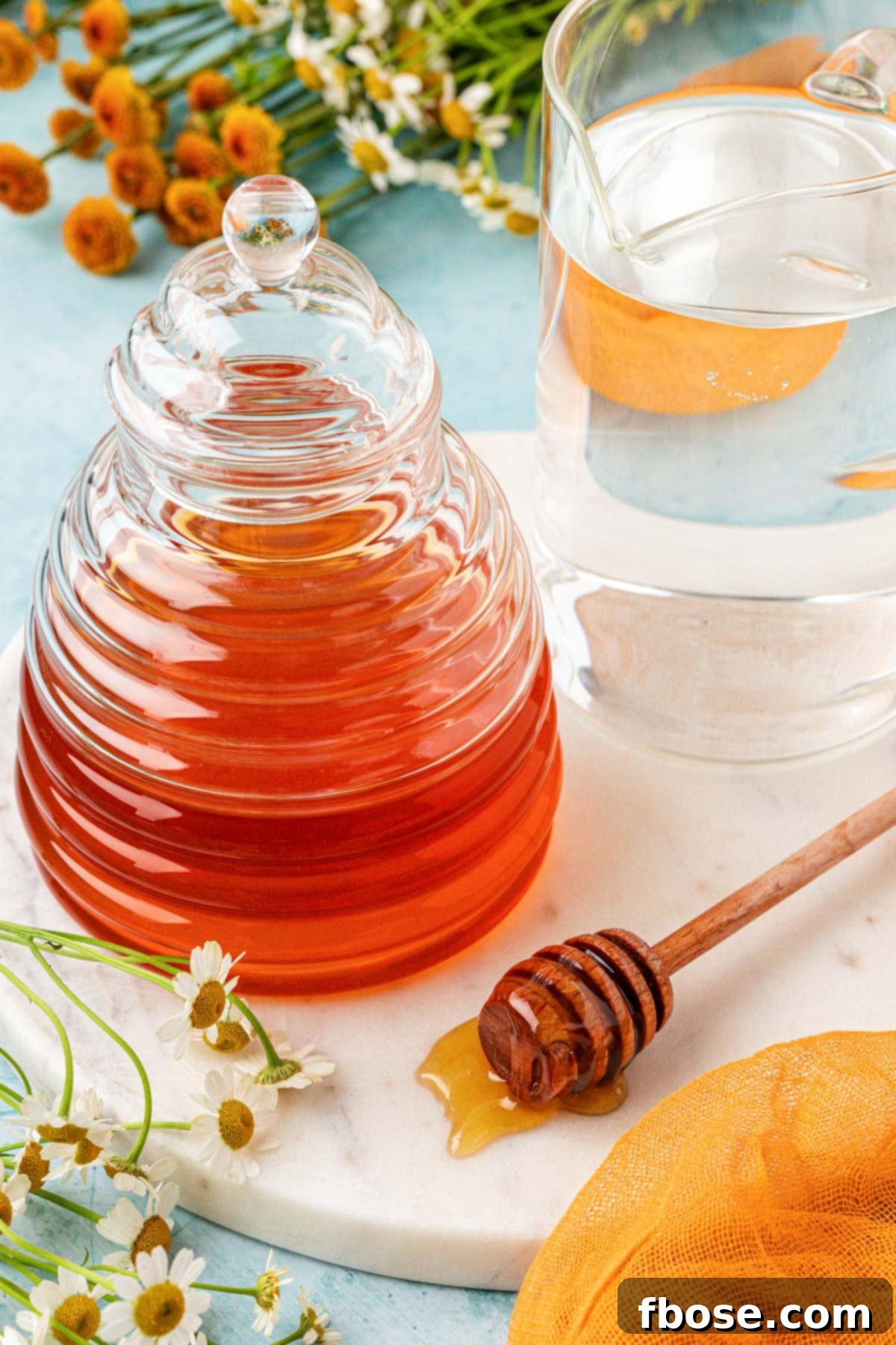 A glass of water next to a glass container of natural honey on a wooden table, highlighting the two simple ingredients for honey simple syrup.