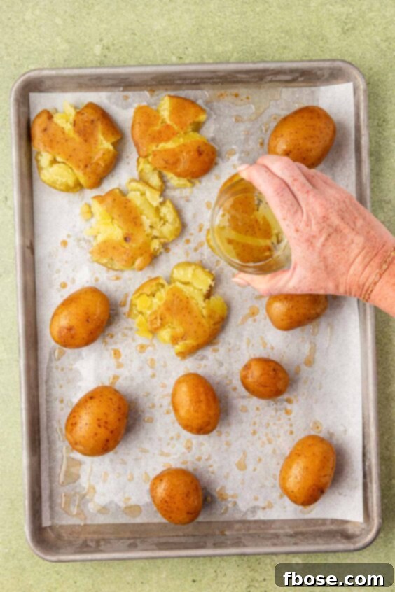 A woman's hand smashing potatoes on a baking pan with the bottom of a glass.