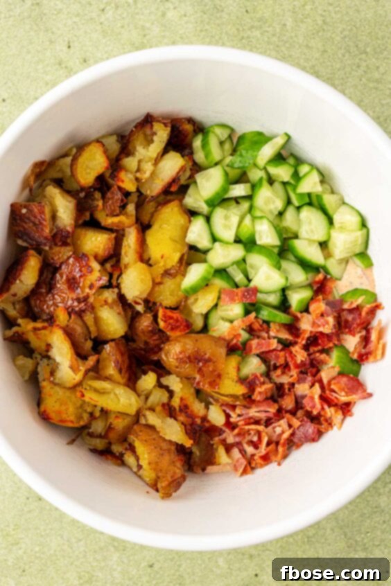 Potatoes, cucumber, and bacon in a white bowl.
