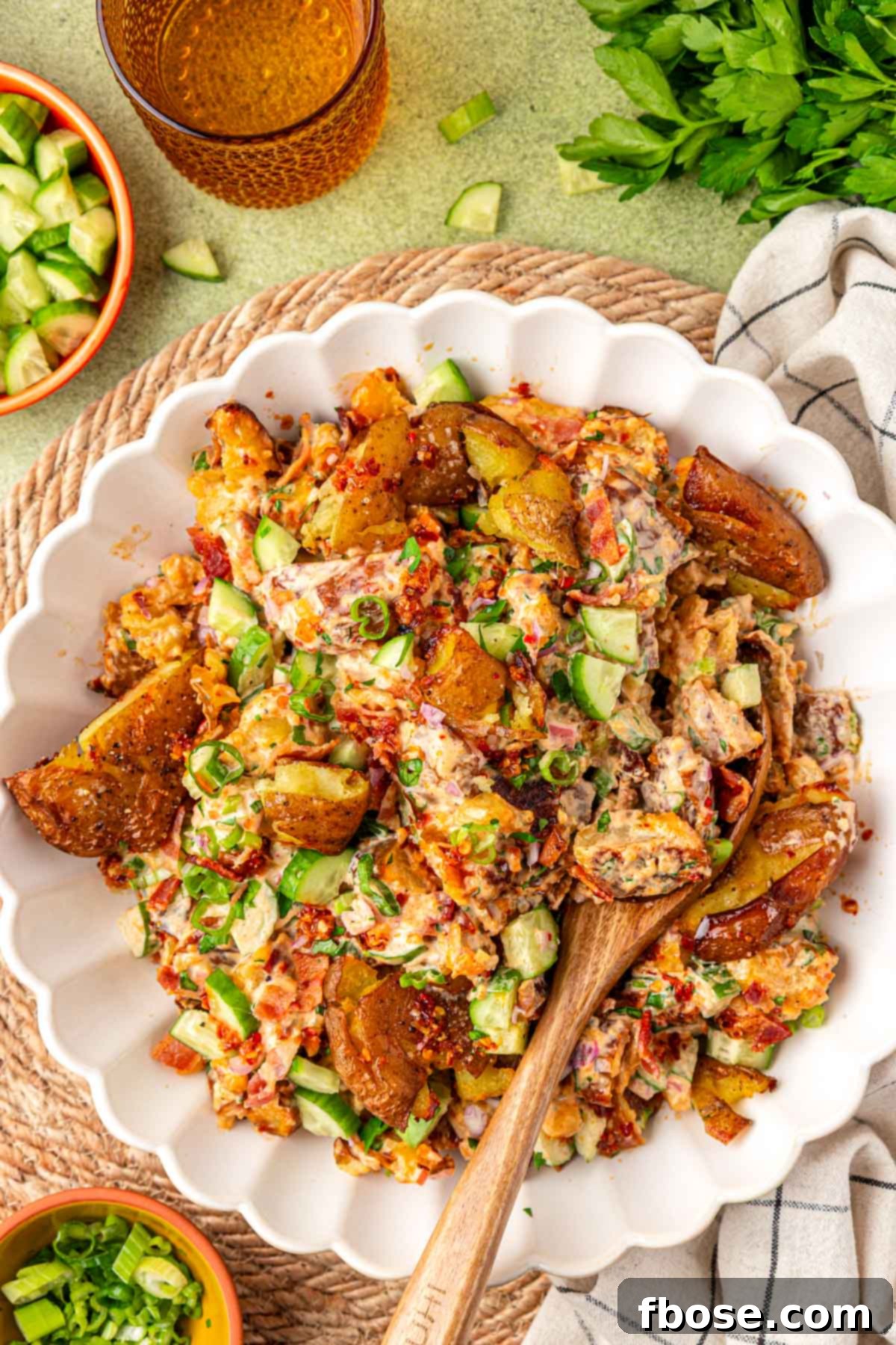 Overhead photo of a white bowl of chili crisp potato salad with a wooden serving spoon in it.