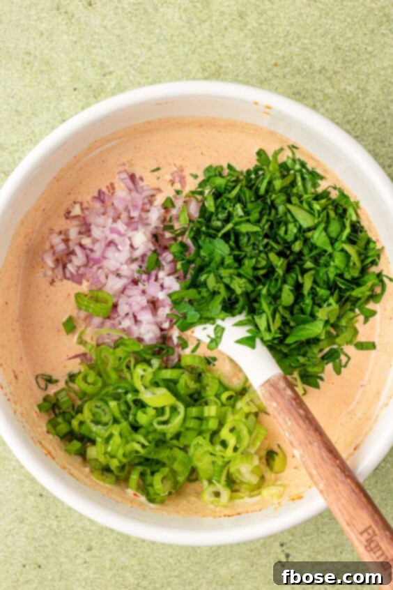 Shallots and herbs being added to a white bowl with a creamy dressing.