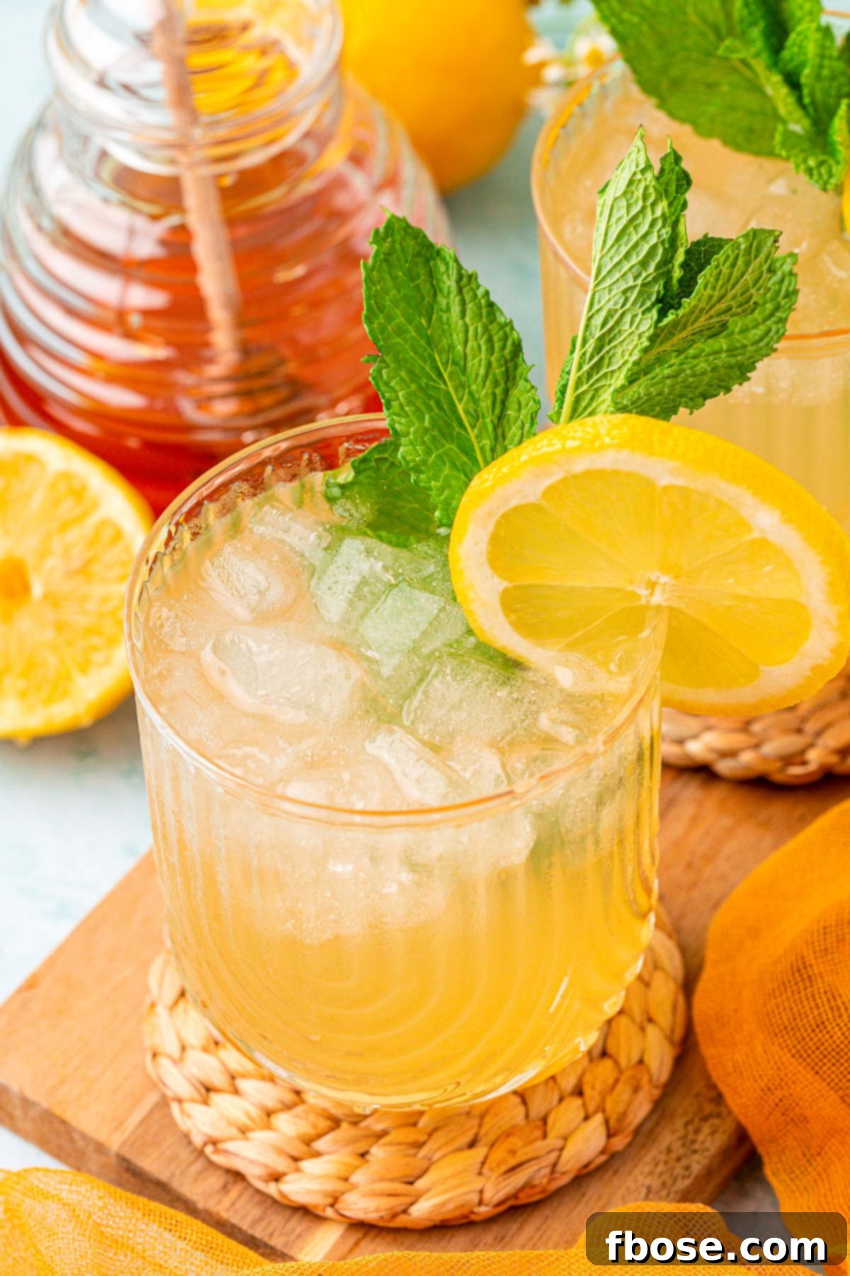 Zesty Honey Delight 7 Two glasses of honey lemonade with lemon slices on a coaster, on a wooden board.