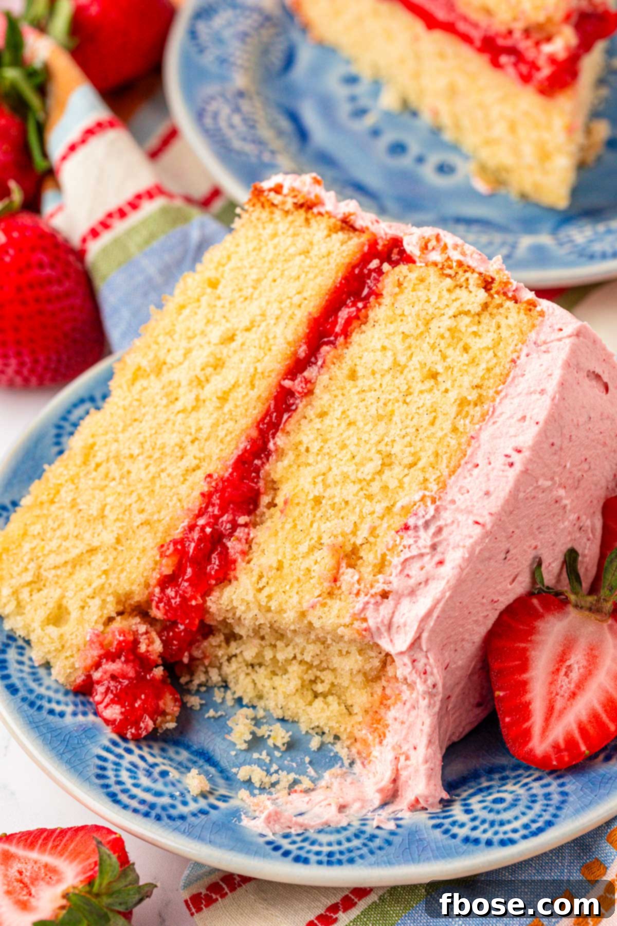 A slice of vanilla cake with strawberry frosting and filling on a blue plate.