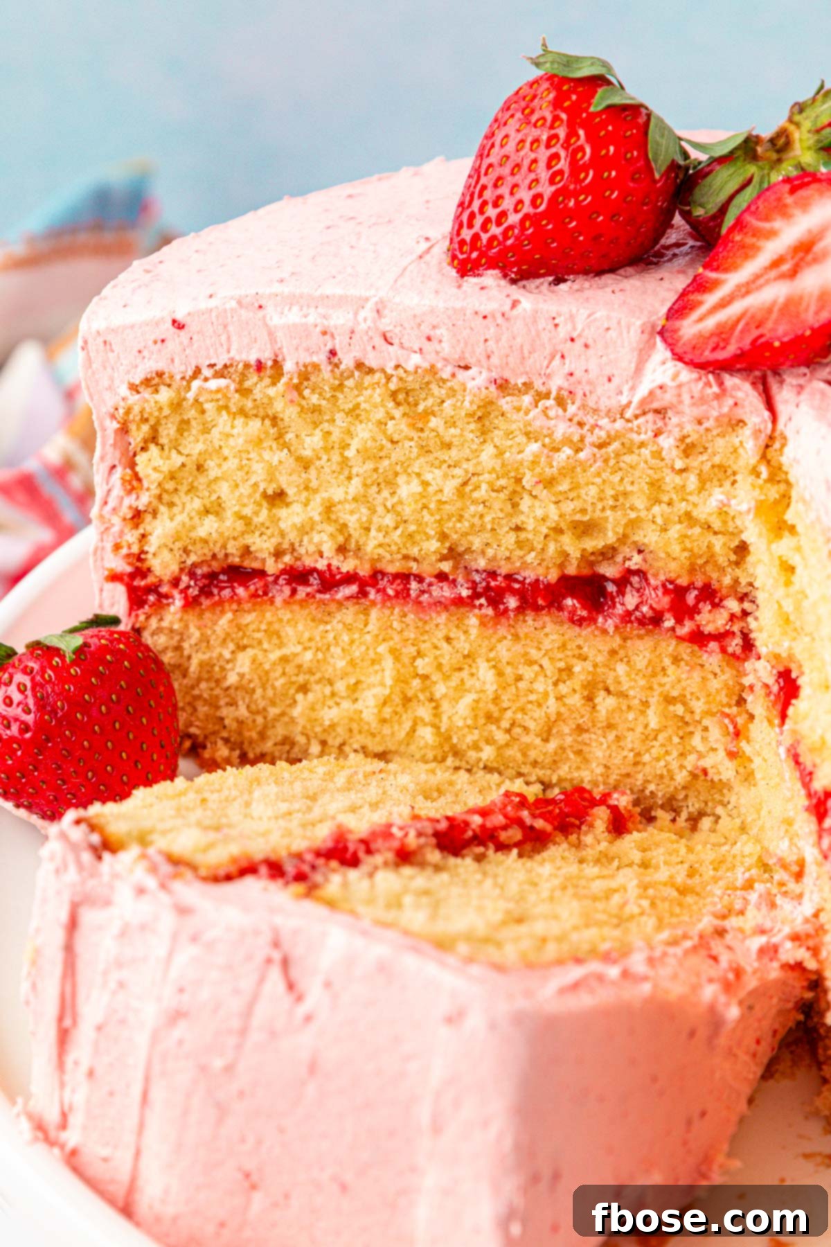 Slice of strawberry cake on a cake stand laying next to the rest of the cake.
