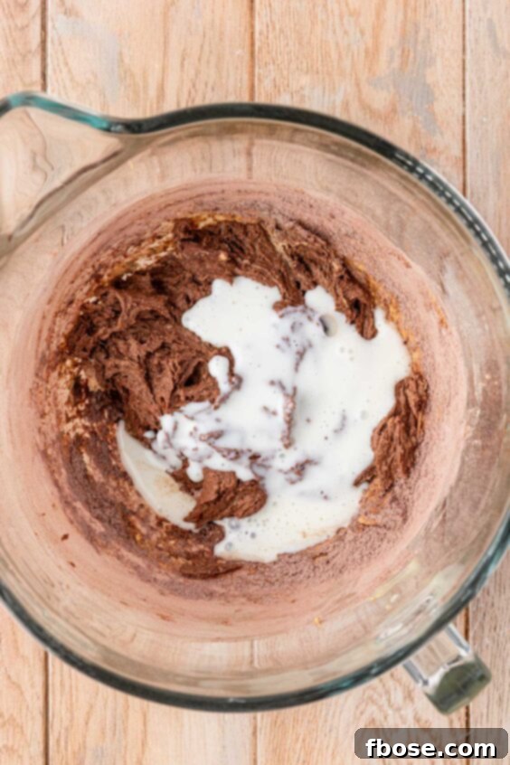 Buttermilk being added to chocolate cake batter in a mixing bowl.