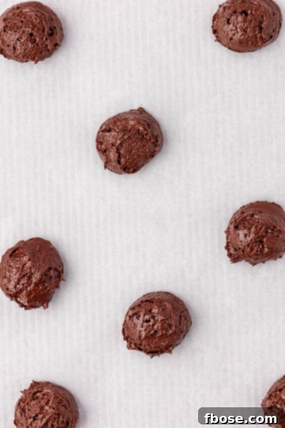 Mounds of chocolate cake batter to make whoopie pies on parchment paper.