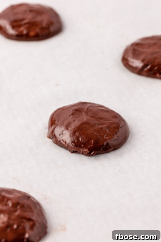 Mounds of chocolate cake batter to make whoopie pies on parchment paper.