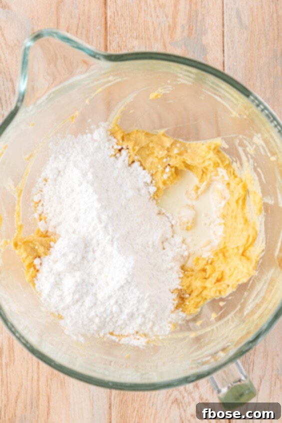Heavy cream and powdered sugar being added to butter in a mixing bowl.