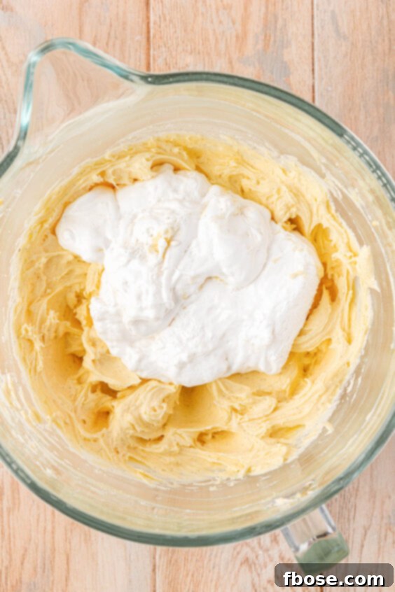 Marshmallow fluff being added to a mixing bowl to make frosting.