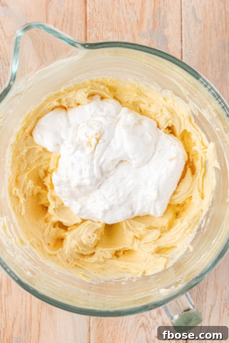 Marshmallow fluff being added to a mixing bowl to make frosting.