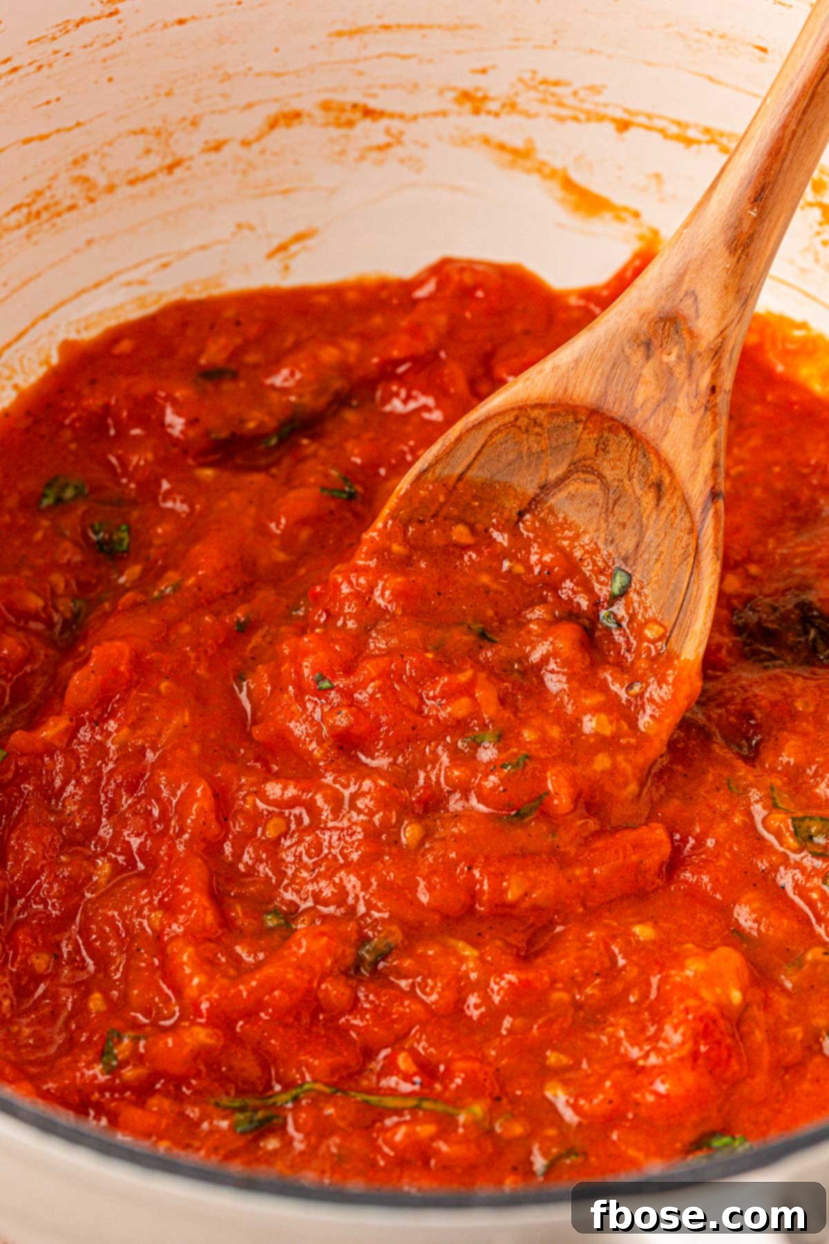 Sun-Kissed Tomato Simplicity 7 Close up of a pot of tomato sauce with a wooden spoon on it.