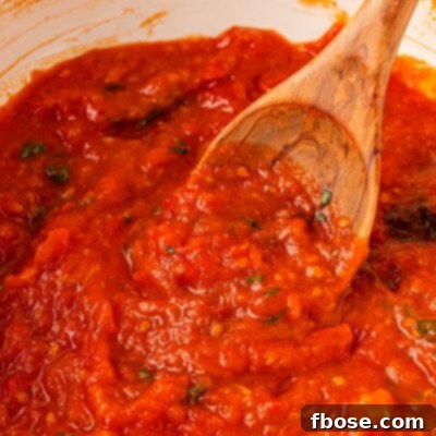Sun-Kissed Tomato Simplicity 8 Close up of a pot of tomato sauce with a wooden spoon on it.