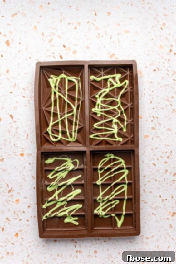 Green colored white chocolate drizzled in a chocolate bar mold.